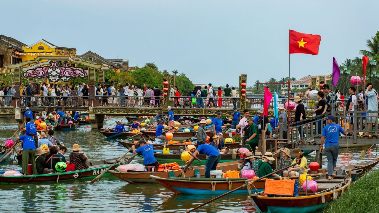 Barcas con faroles en el río Thu Bon en Hoi An, Vietnam, bajo una bandera vietnamita