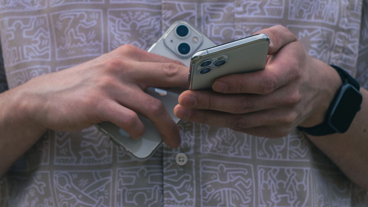 A person holding two smartphones side by side, comparing them