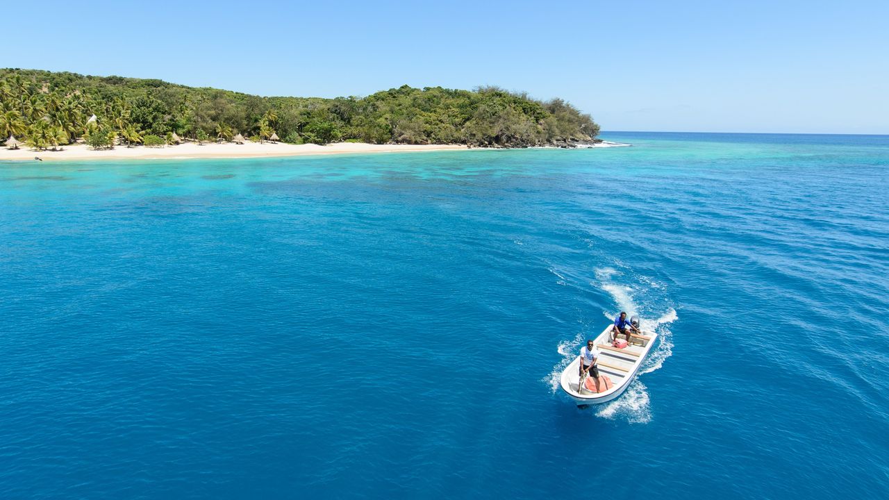 A small boat crossing turquoise water towards a palm covered island