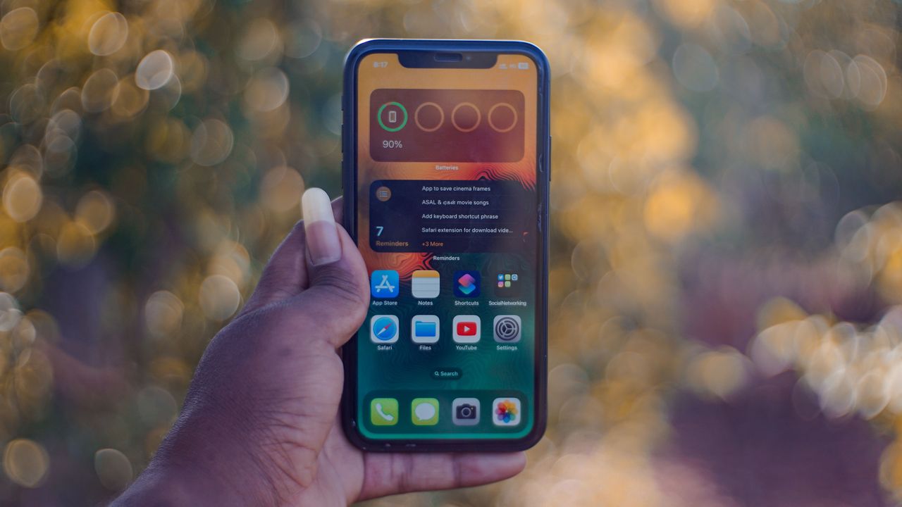 Mano sosteniendo un iPhone con la pantalla de inicio al aire libre