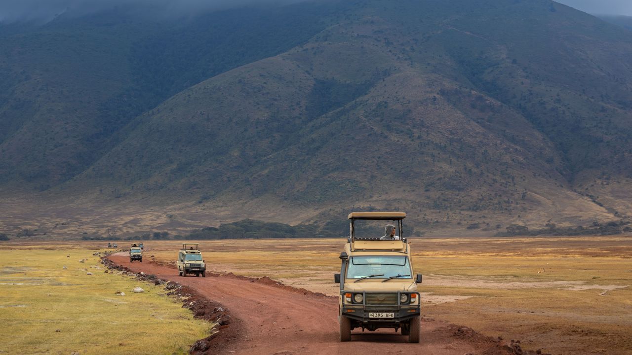 Un jeep de safari en un camino de tierra roja por el fondo del cráter del Ngorongoro en Tanzania, con la pared del cráter detrás