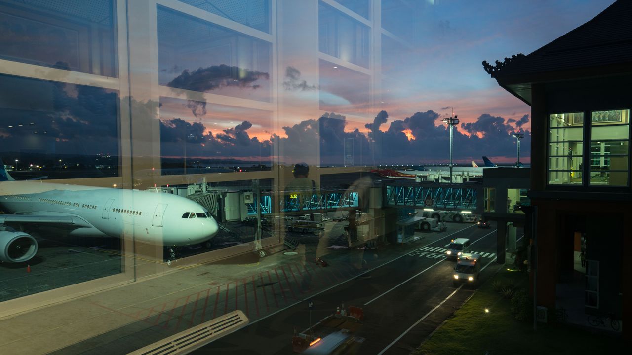 An airliner at a gate seen through a terminal window at dusk