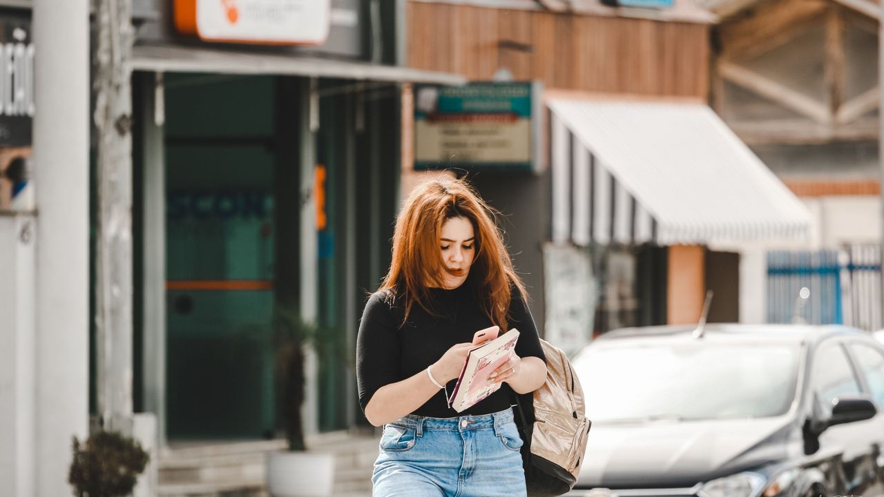 A woman with a backpack checks her phone on a city street lined with shops
