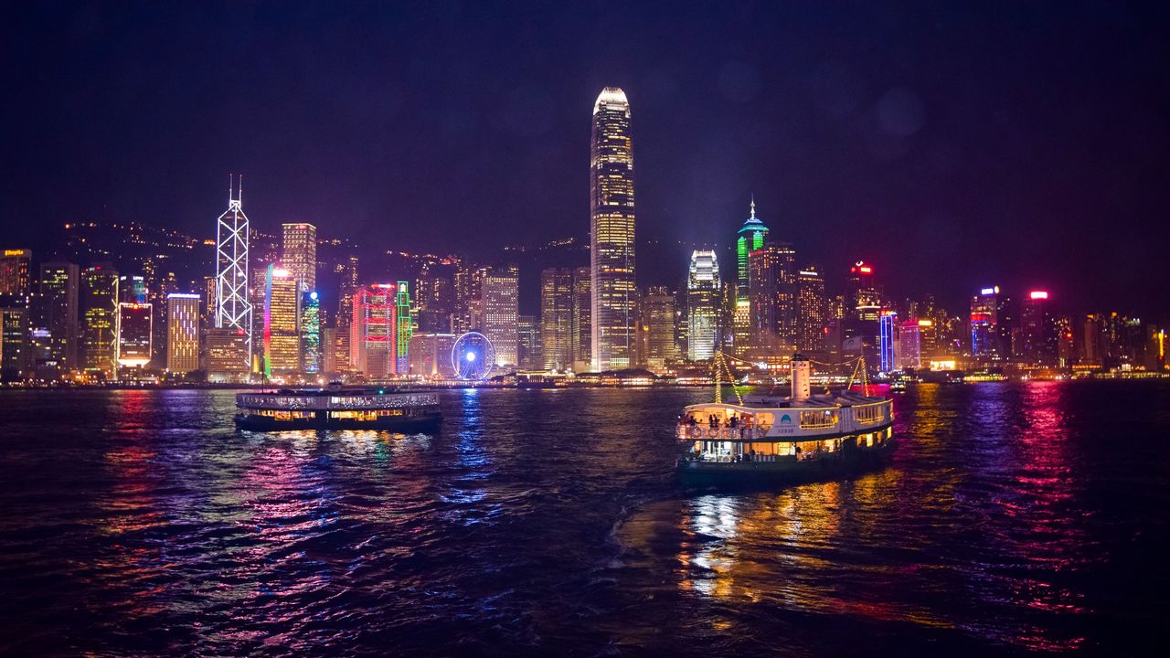 El puerto Victoria de noche con el horizonte de Hong Kong iluminado y ferris cruzando