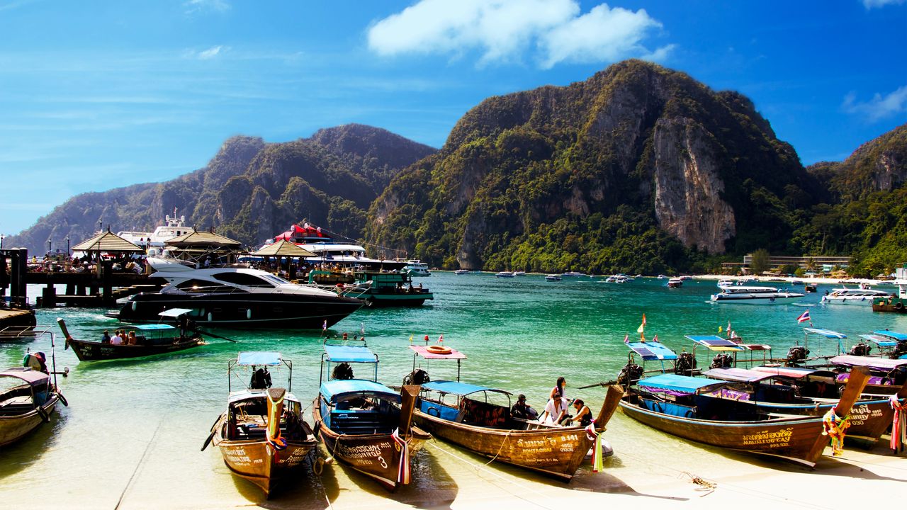 Botes de cola larga en una playa de arena blanca bajo cerros de piedra caliza verdes en el sur de Tailandia