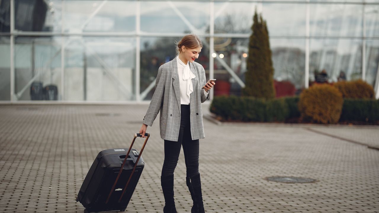 Viajera con una maleta mirando su teléfono fuera de una terminal de aeropuerto