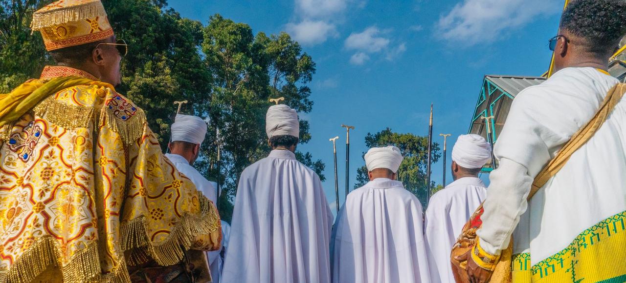 Men in traditional Ethiopian attire participating in a religious ceremony outdoors, under a clear blue sky