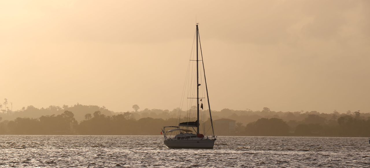 A serene sailboat drifting on the ocean against a warm sunset in French Guiana