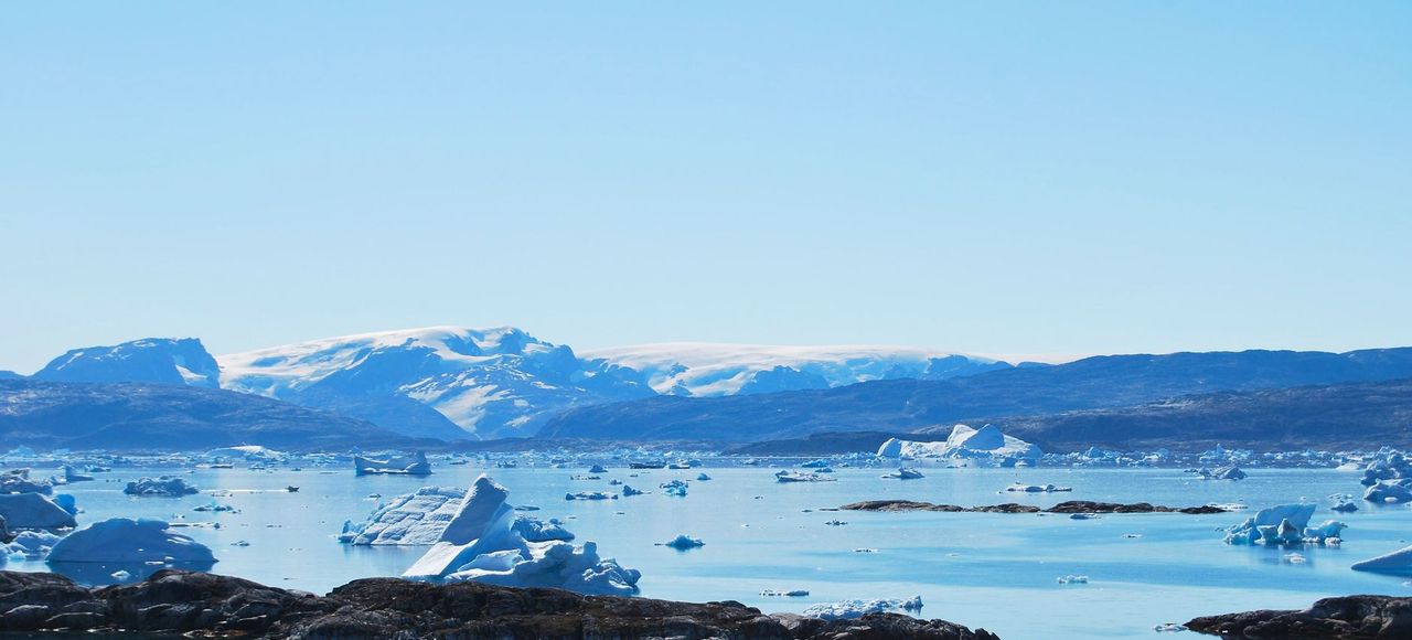 A breathtaking view of icebergs floating in a tranquil sea with distant snow-capped mountains, captured in Greenland