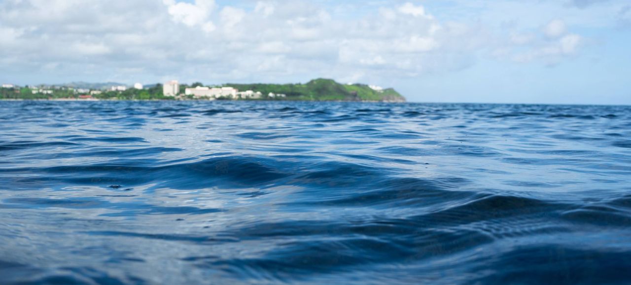 Guam: Serene ocean scene with Tumon Bay in the background, showcasing clear blue waters and sky