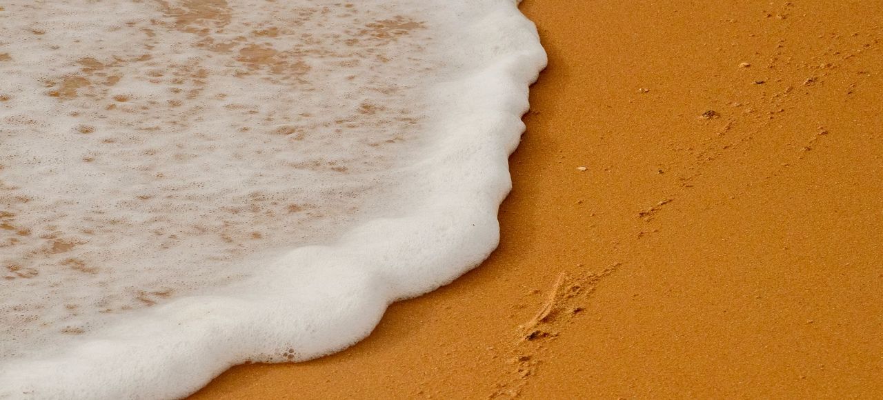 Guyana: Close-up of ocean waves meeting golden sand on a Guyanese beach