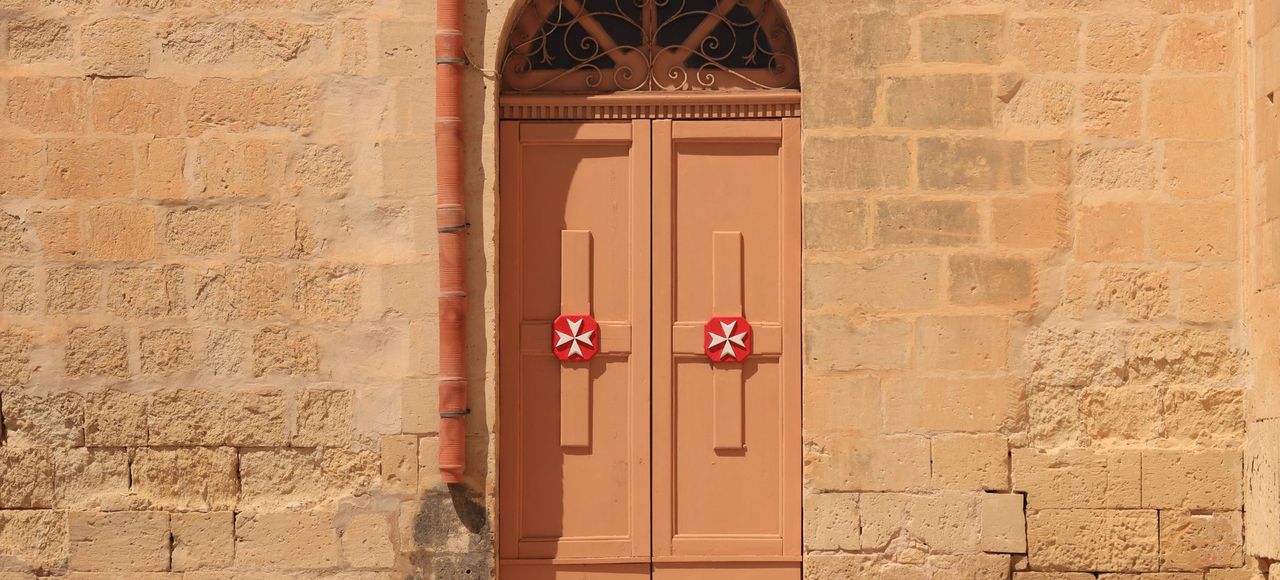Charming door with Maltese cross on a historic stone building in Valletta, Malta