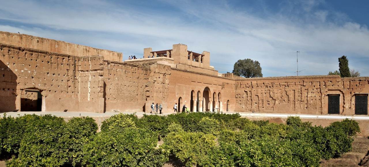 View of historic red walls and lush gardens under a blue sky in Marrakesh, Morocco
