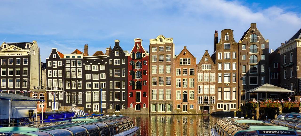 Netherlands: Colorful historic buildings along Amsterdam canals with boats in the foreground, reflecting in calm water