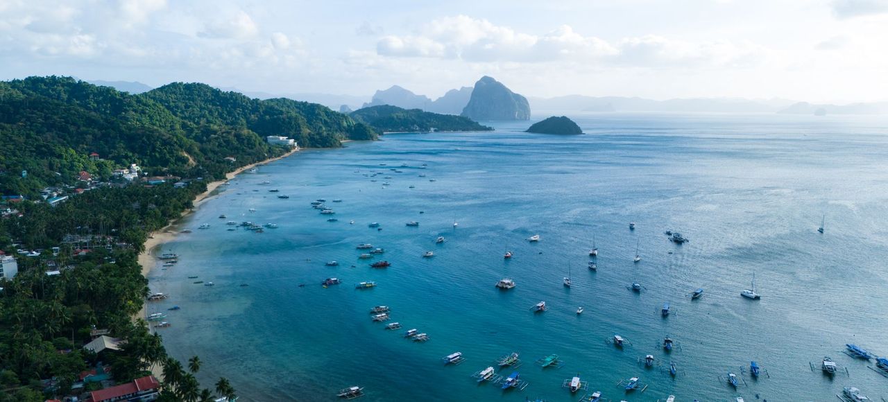 Stunning aerial view of El Nido's vibrant blue bay with lush greenery and boats, capturing the essence of the Philippines' natural beauty