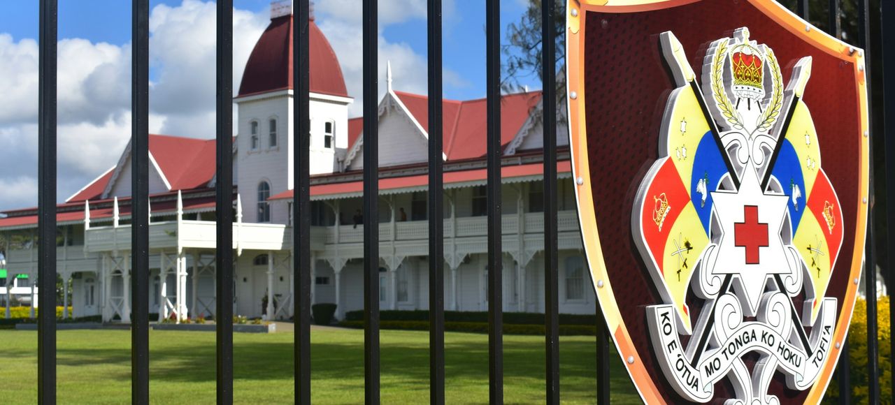 Tonga: Building with red roof behind a fence displaying an emblem