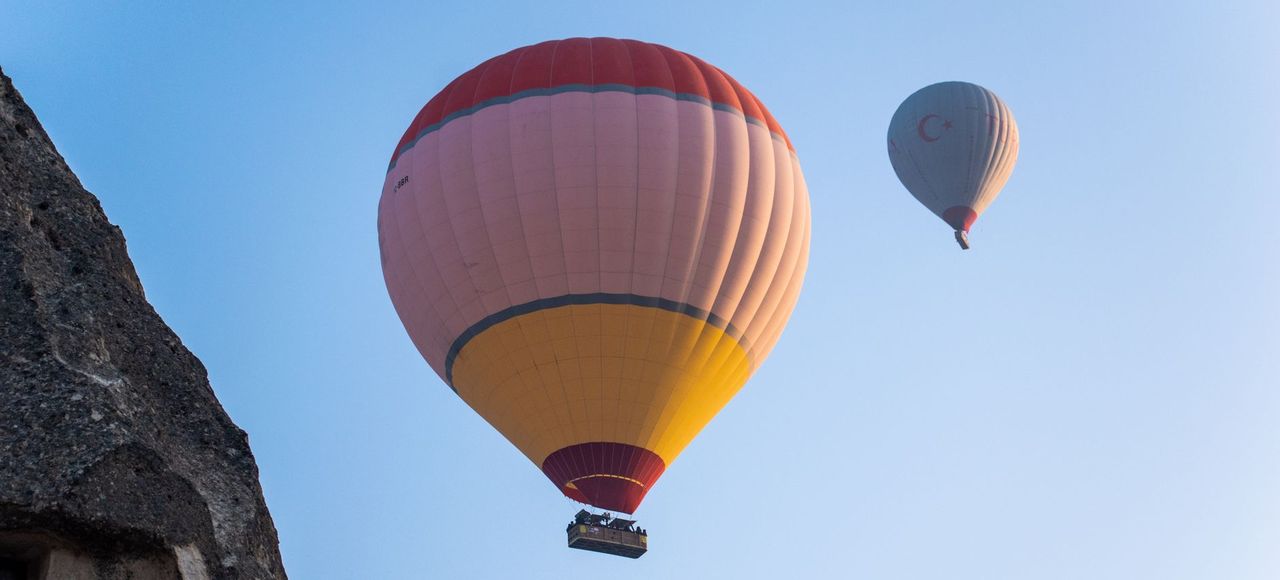 Türkiye: Two hot air balloons soar over a rocky landscape under a clear blue sky, capturing adventure and travel vibes